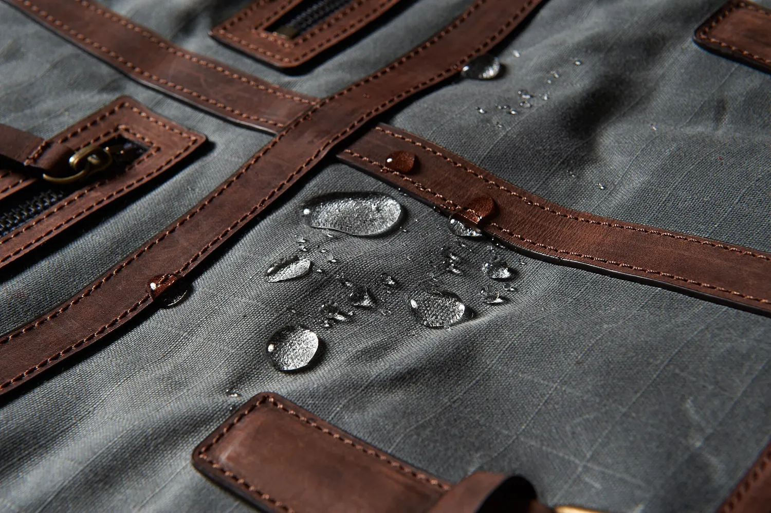 Drops of water standing on the grey surface of waxed canvas with brown leather straps