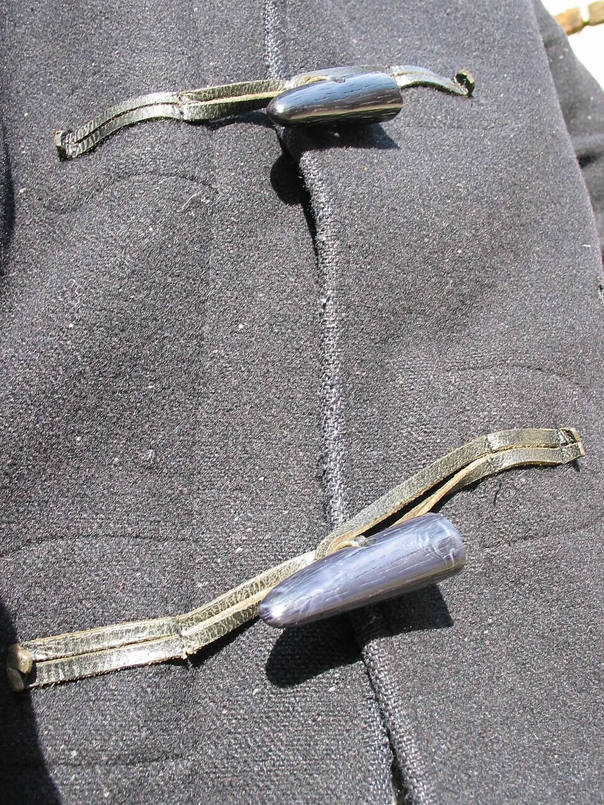 Two toggles on cord loops closing the front of a grey wool duffle coat